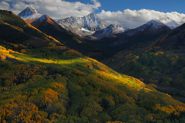 Late afternoon clouds retreat from the high peaks of the Elk Mountains, leaving a fresh dusting of snow on Capitol Peak. In the valley below, aspen trees begin their transformation from a deep shade of green to the vibrant gold they are so famous for.